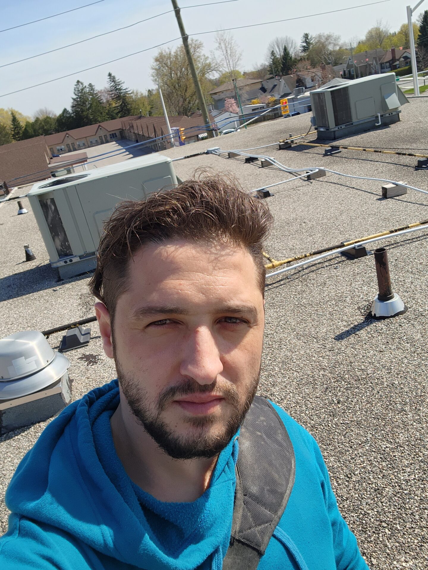 Abdullah Ghzail HVAC technician surveying a flat commercial roof with multiple packaged rooftop HVAC units in the background.