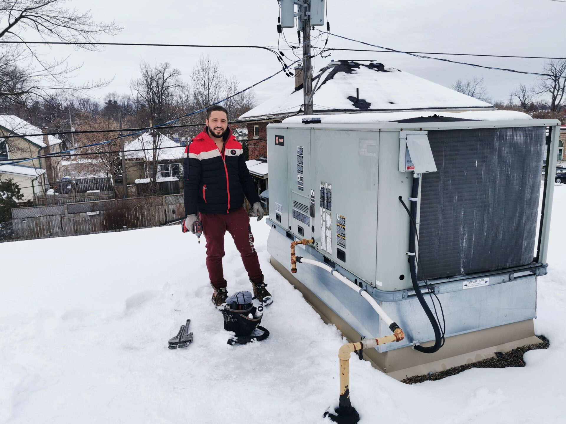 Abdullah Ghzail the Commercial HVAC technician standing beside an active Trane rooftop heating unit during severe winter snow conditions.