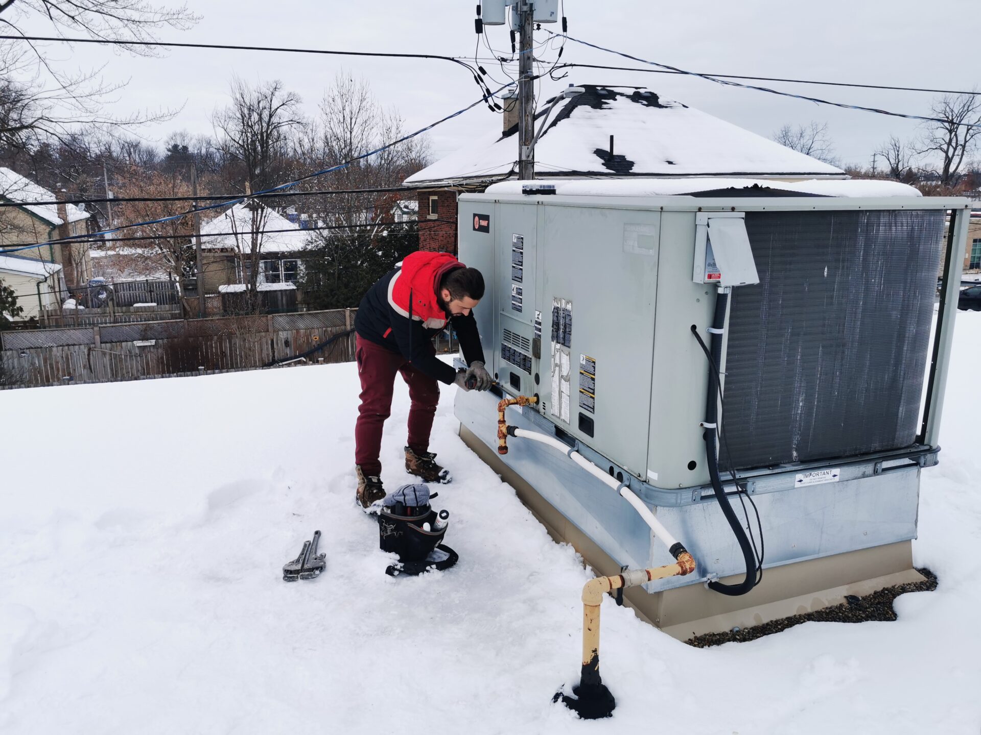 HVAC specialist Abdullah Ghzail troubleshooting a Trane commercial rooftop heating unit on a snowy roof during winter.