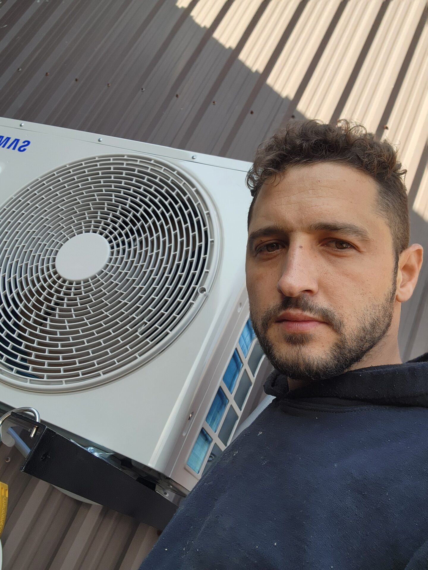 Abdullah Ghzail, owner of Hawana HVAC Solutions, standing next to a newly installed Samsung ductless heat pump outdoor unit.