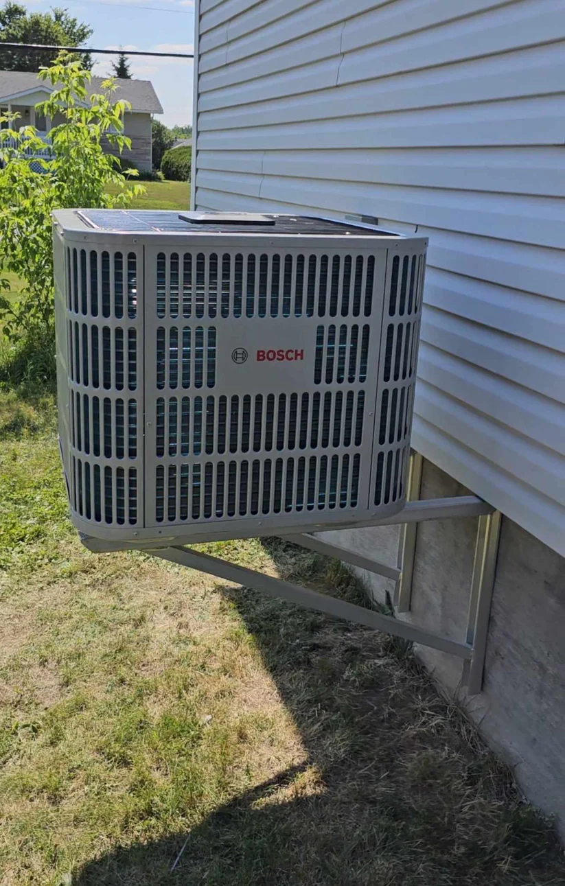 Bosch IDS ducted heat pump condenser unit installed outdoors on a heavy-duty wall mount bracket next to vinyl siding