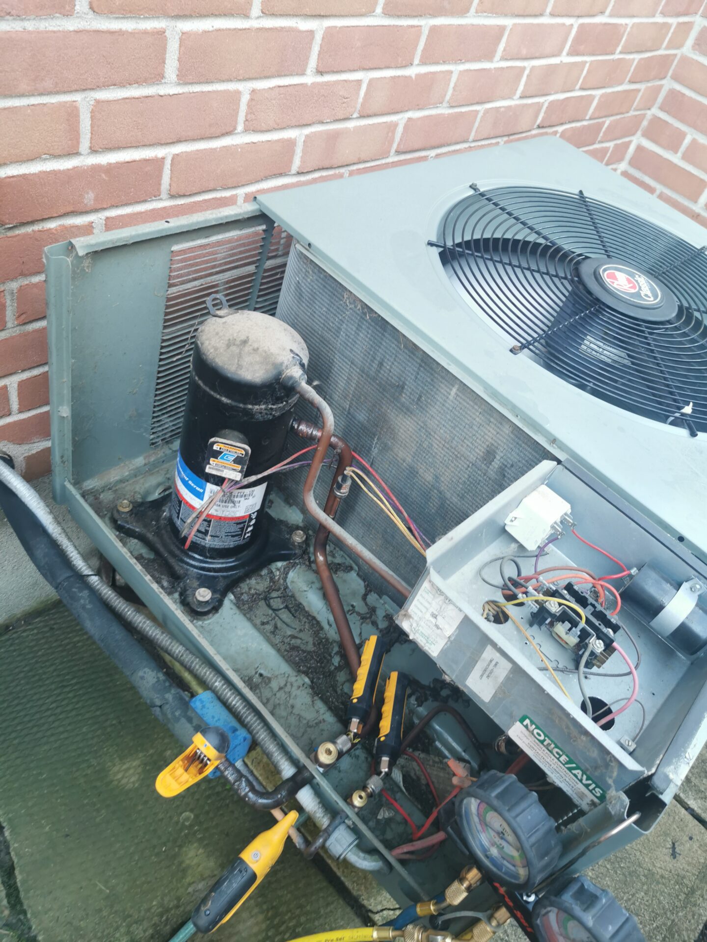 An outdoor air conditioning condenser with side panels removed, exposing the scroll compressor, dual run capacitor, and wiring contactor.