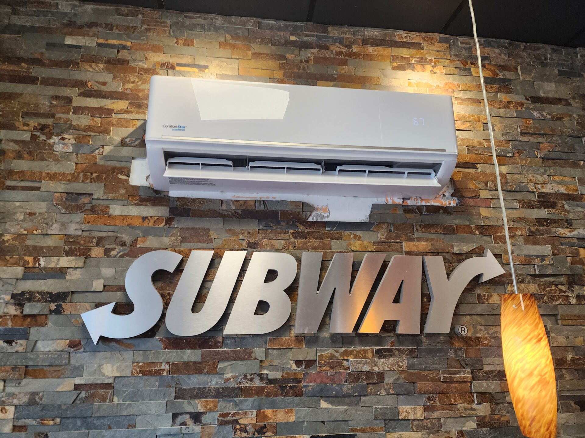 ComfortStar ductless air conditioning indoor unit installed on a stone wall above a Subway restaurant sign