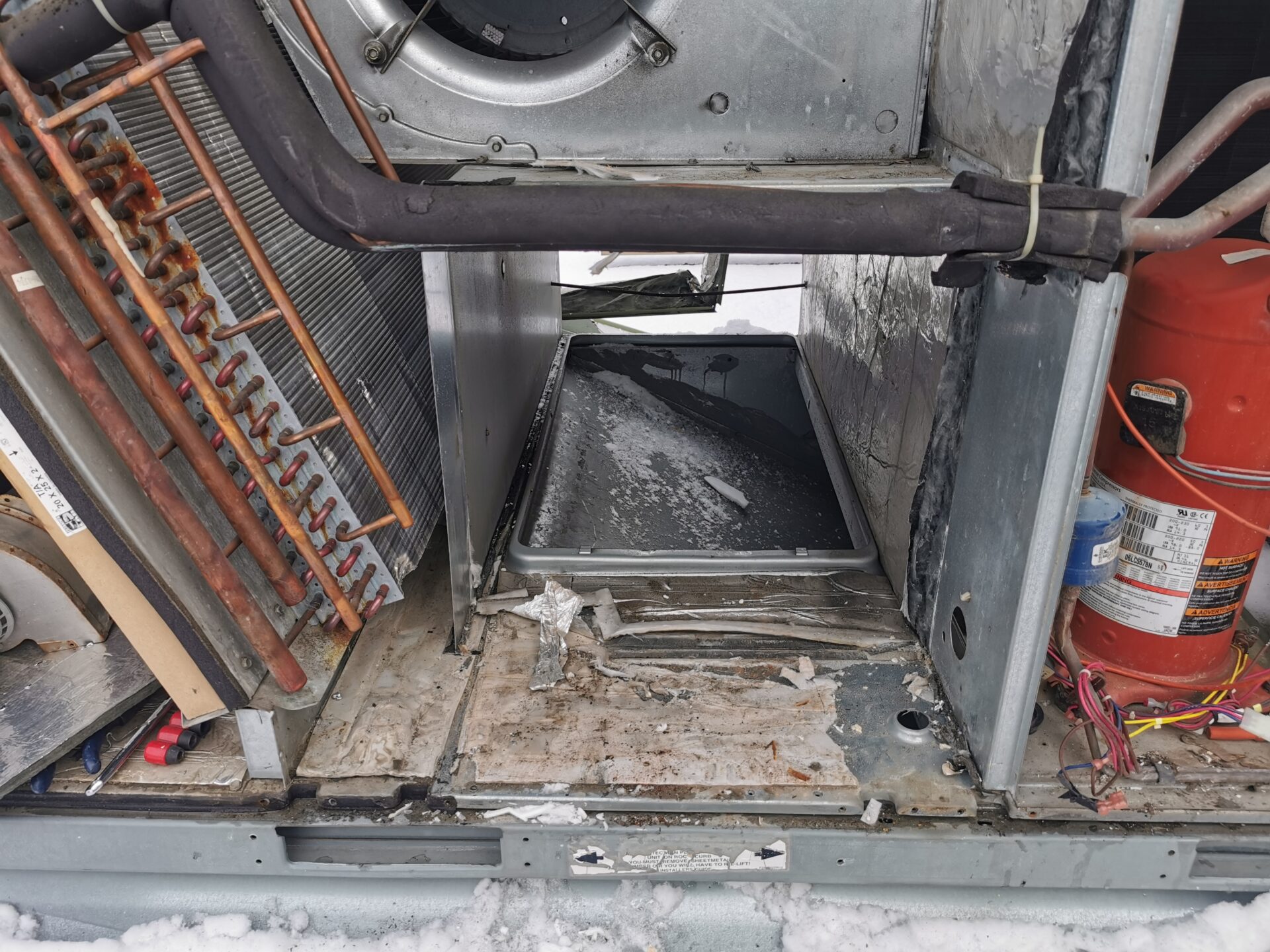 Internal view of a commercial rooftop HVAC unit showing the evaporator coil and compressor during a winter service inspection.