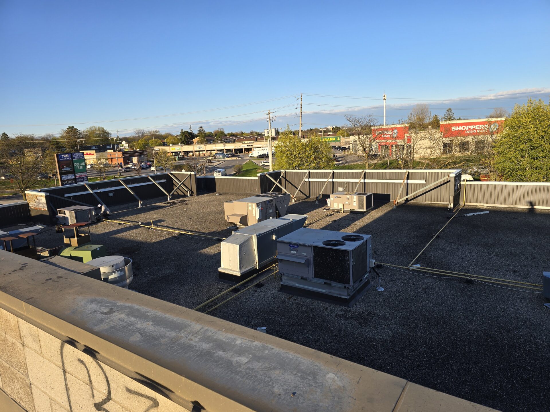 A wide view of a commercial building's flat roof featuring multiple rooftop HVAC units (RTUs) with a retail plaza in the background.