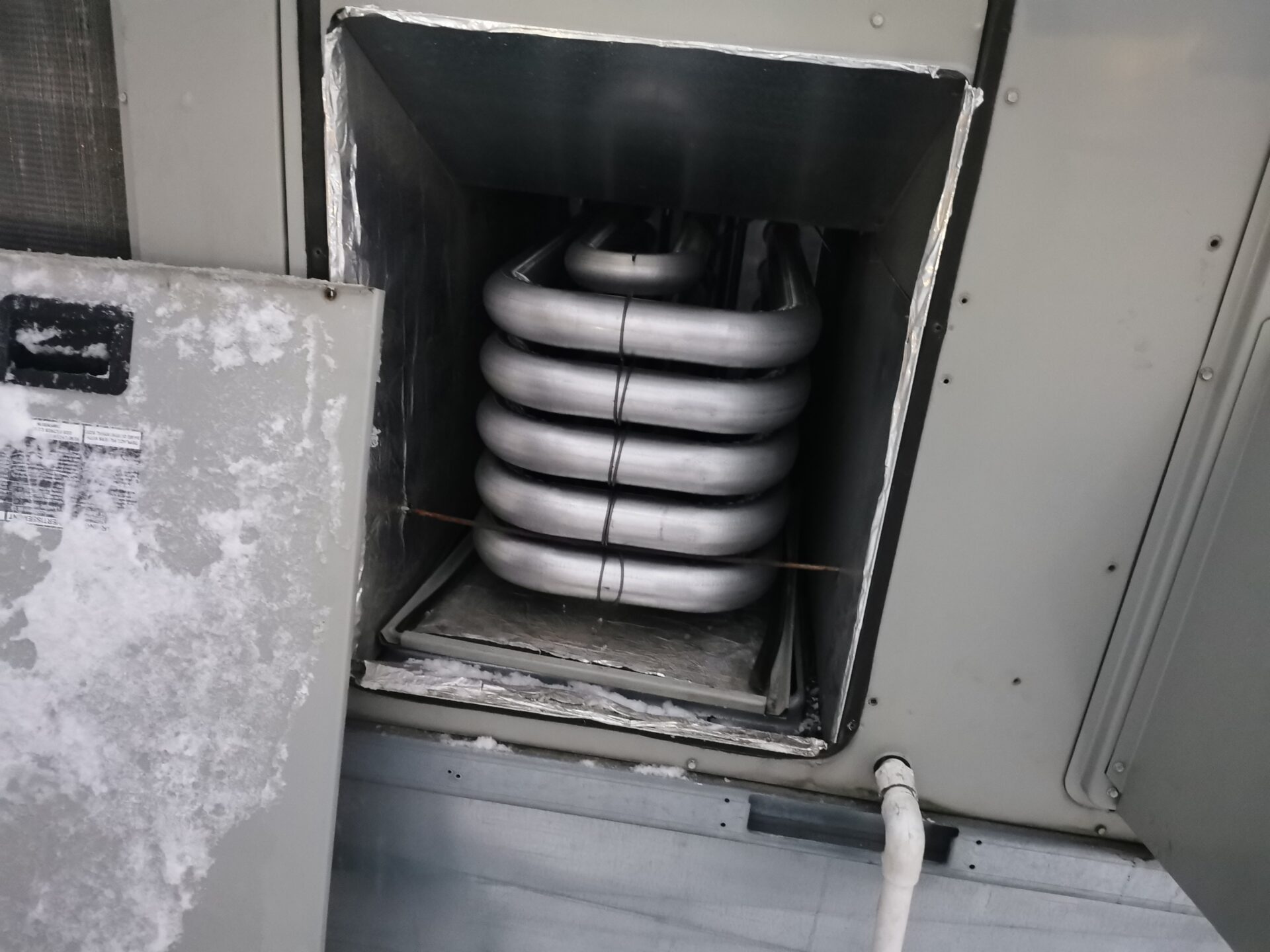 Close-up view of an exposed stainless steel tubular gas heat exchanger inside a commercial rooftop HVAC unit.