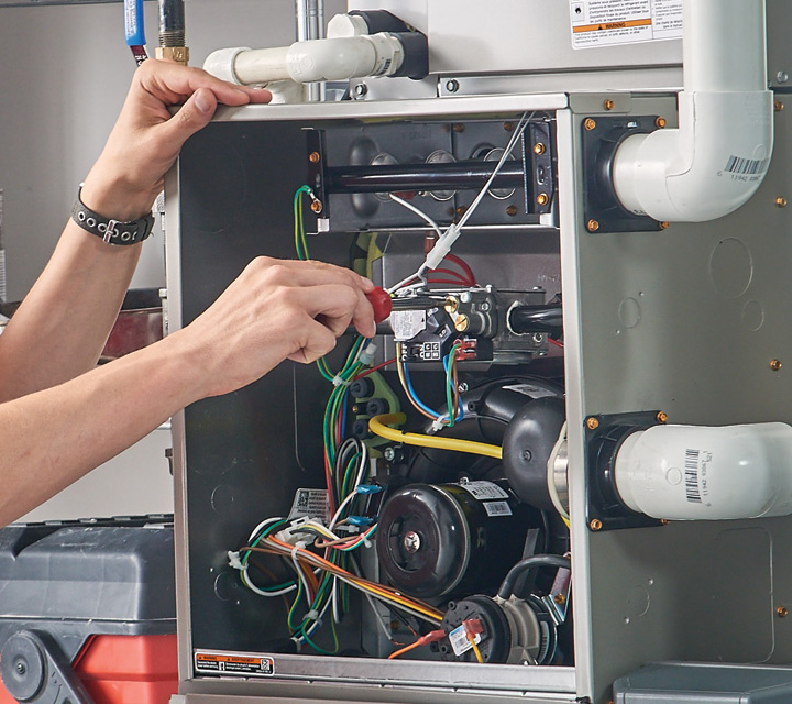 A skilled HVAC technician's hands using a screwdriver to perform detailed repairs on the internal electrical components and gas valve of an open furnace.