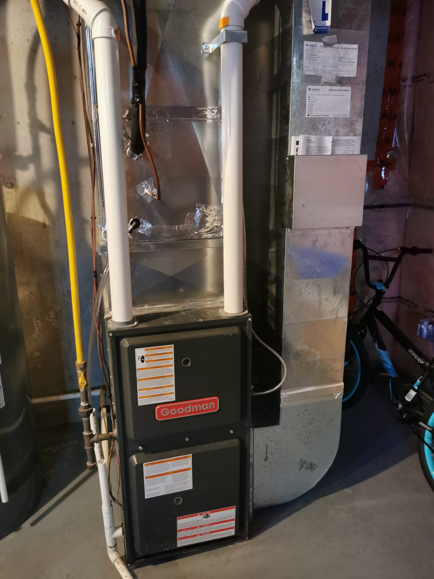 A cleanly installed Goodman high-efficiency gas furnace in a residential basement with sealed ductwork and white PVC exhaust venting.