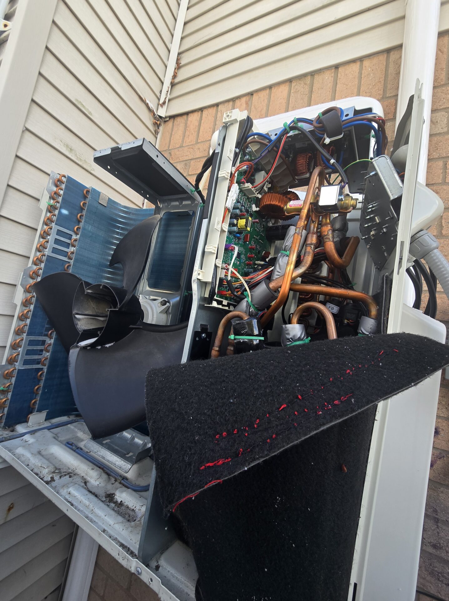 A ductless mini-split outdoor unit completely stripped down, exposing the internal copper coils, compressor, and the complex electronic inverter control board.