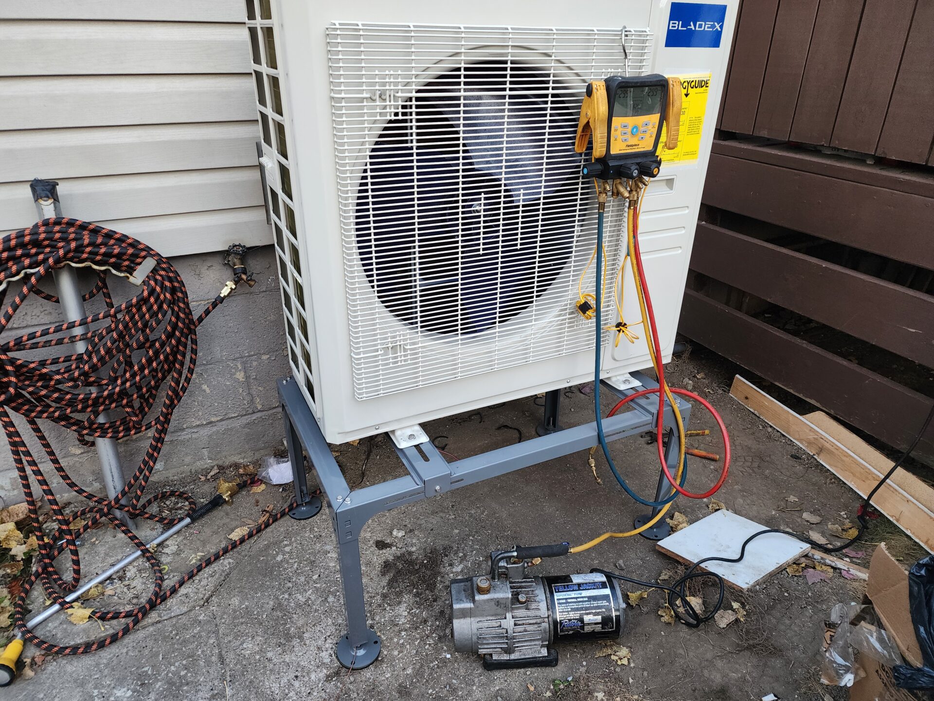 Digital manifold gauges and a vacuum pump pulling a deep vacuum on a Bladex heat pump condenser during installation.