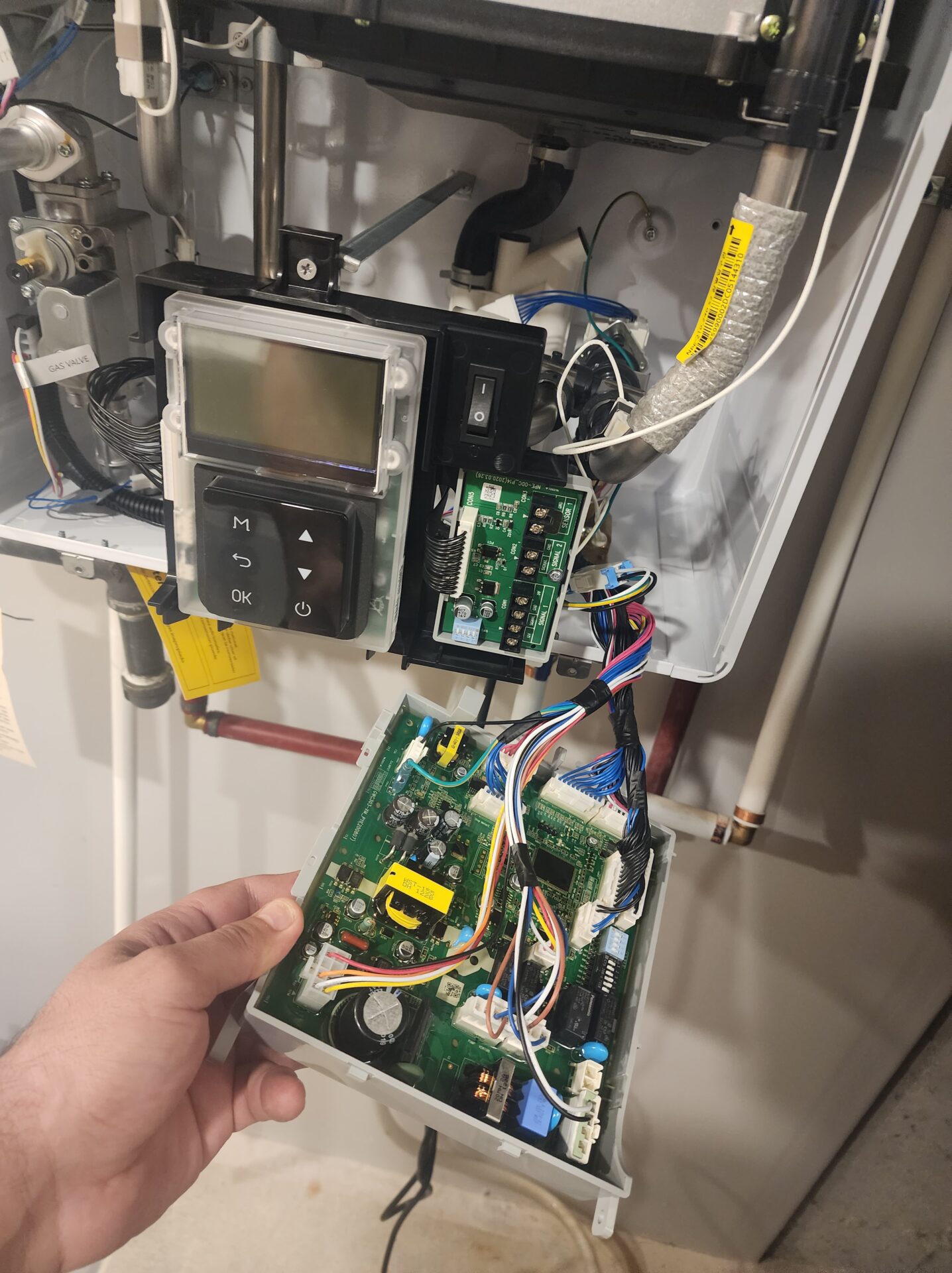 Technician replacing the main electronic control board on a wall-mounted Navien tankless water heater.