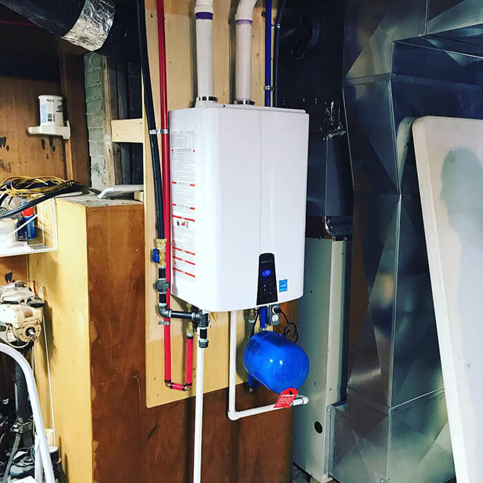 A professionally installed Navien tankless water heater mounted securely on a wooden backboard, complete with neatly organized PEX piping, secure gas lines, and a blue thermal expansion tank.