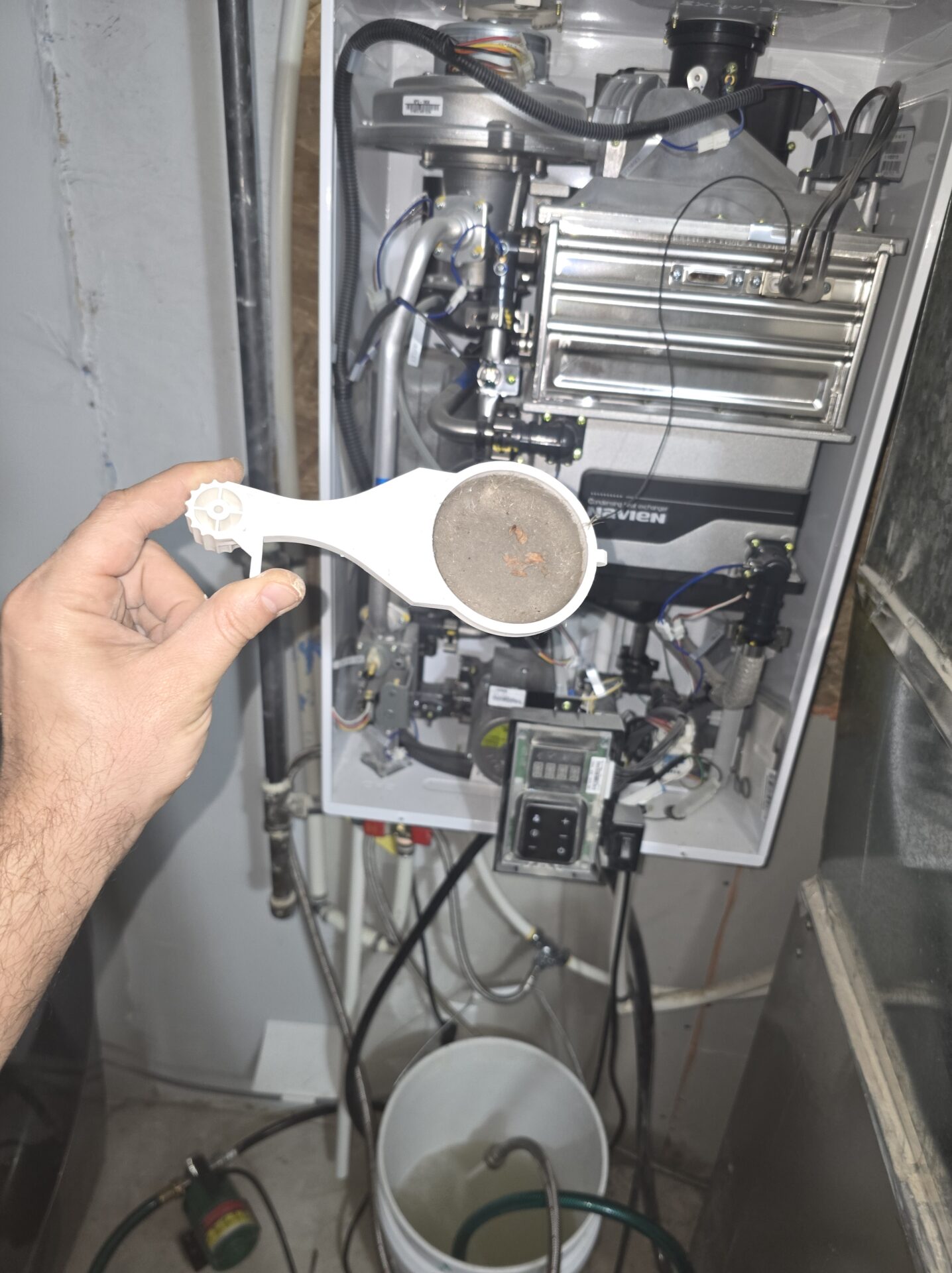 A hand holding a heavily clogged air intake filter removed from a high-efficiency navien tankless water heater.
