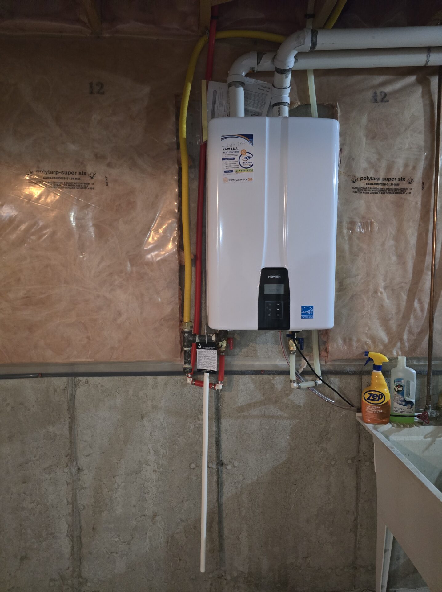 Newly installed Navien tankless water heater mounted cleanly on a basement wall, featuring a Hawana HVAC Solutions service sticker