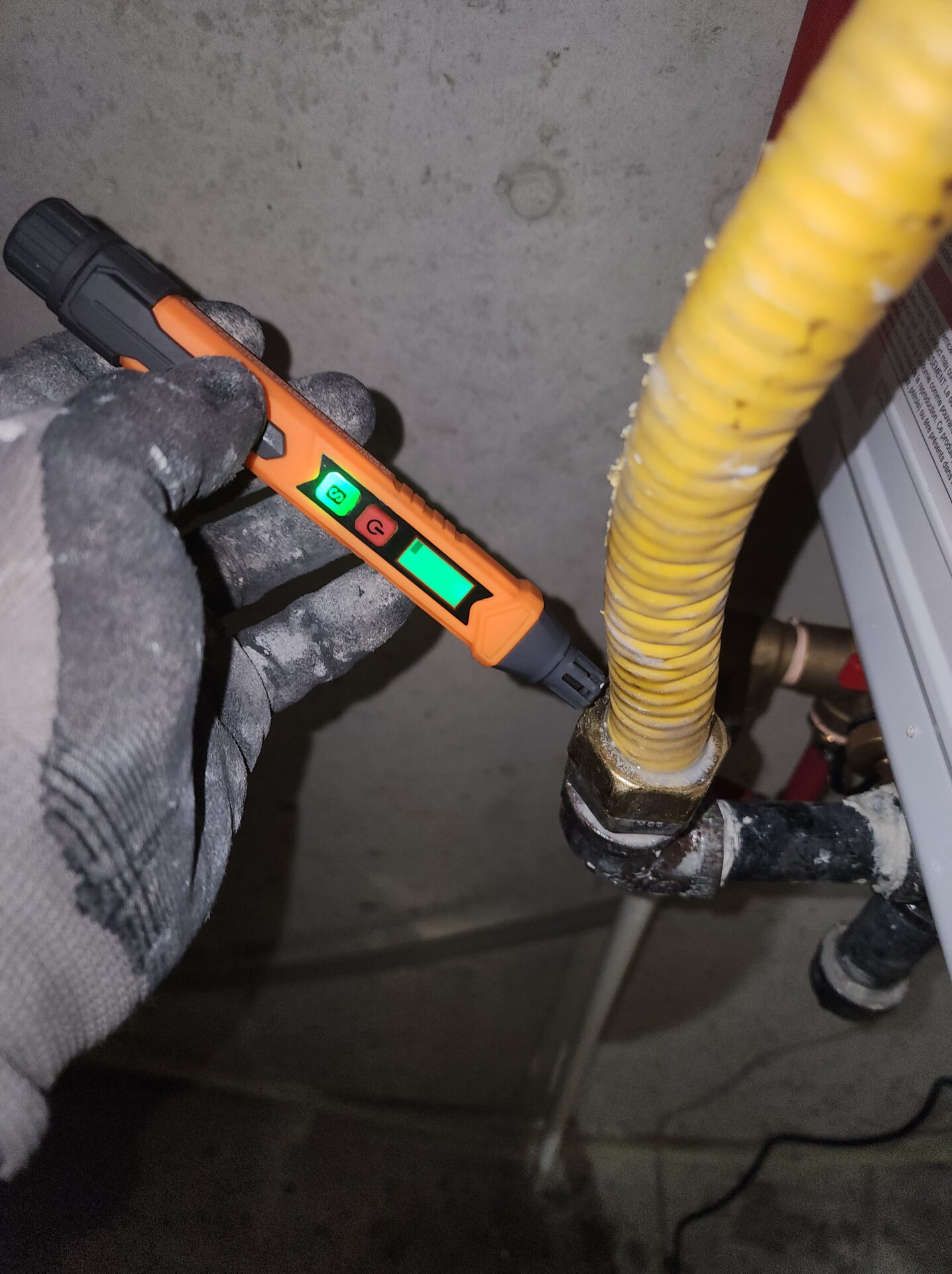 Technician using a digital combustible gas leak detector pen on a yellow corrugated residential gas pipe.