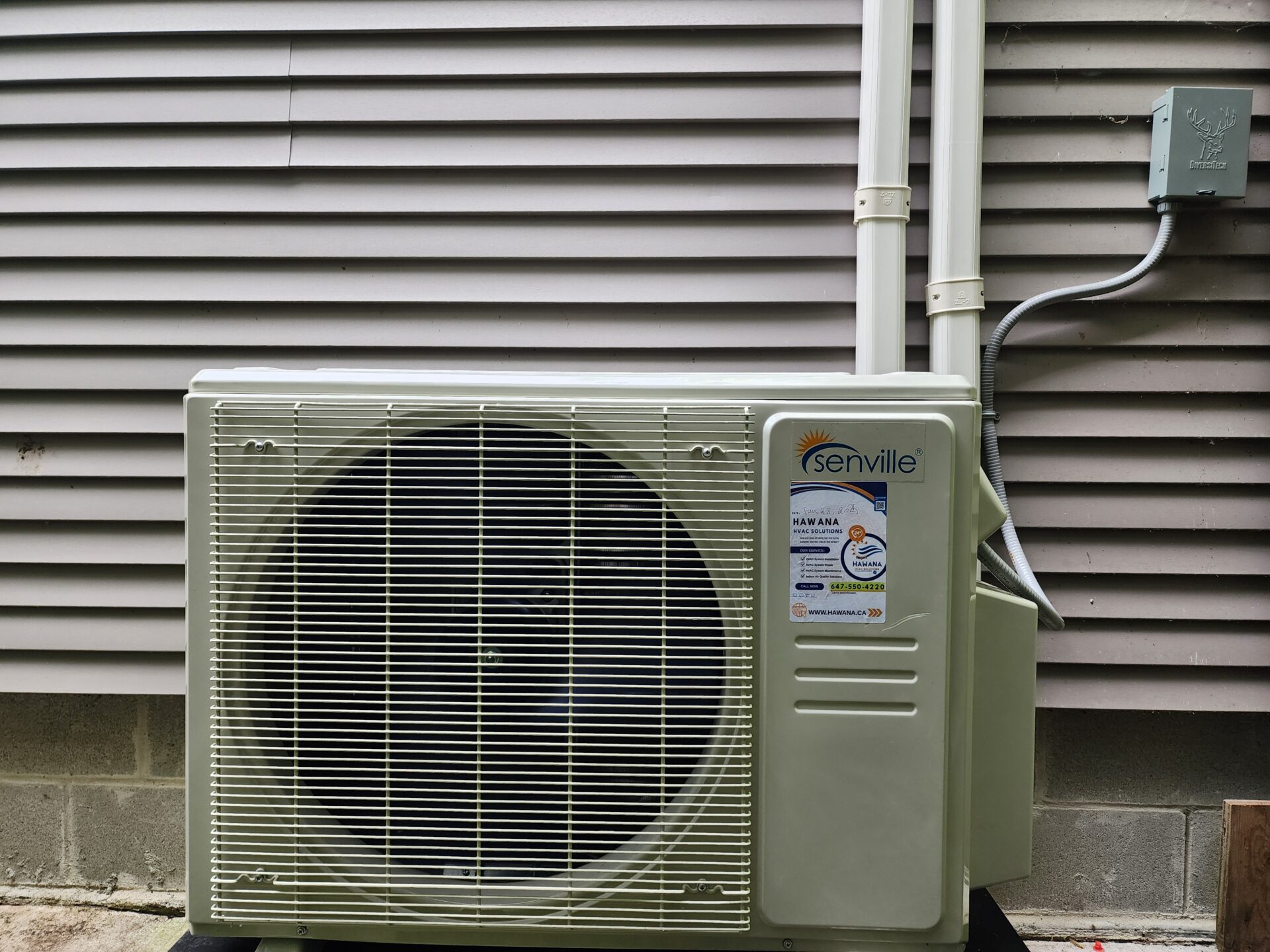 A Senville ductless heat pump outdoor condenser unit installed next to a home's siding with a Hawana HVAC Solutions service sticker applied.