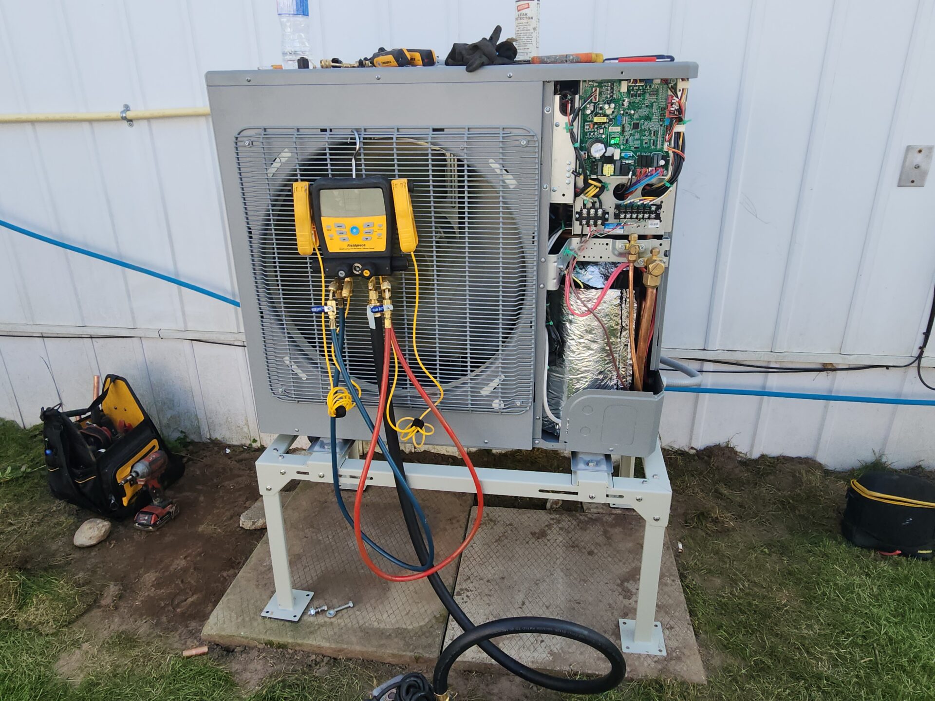 A side-discharge cold climate heat pump mounted on a raised metal ground stand with Fieldpiece digital manifold gauges connected for testing.