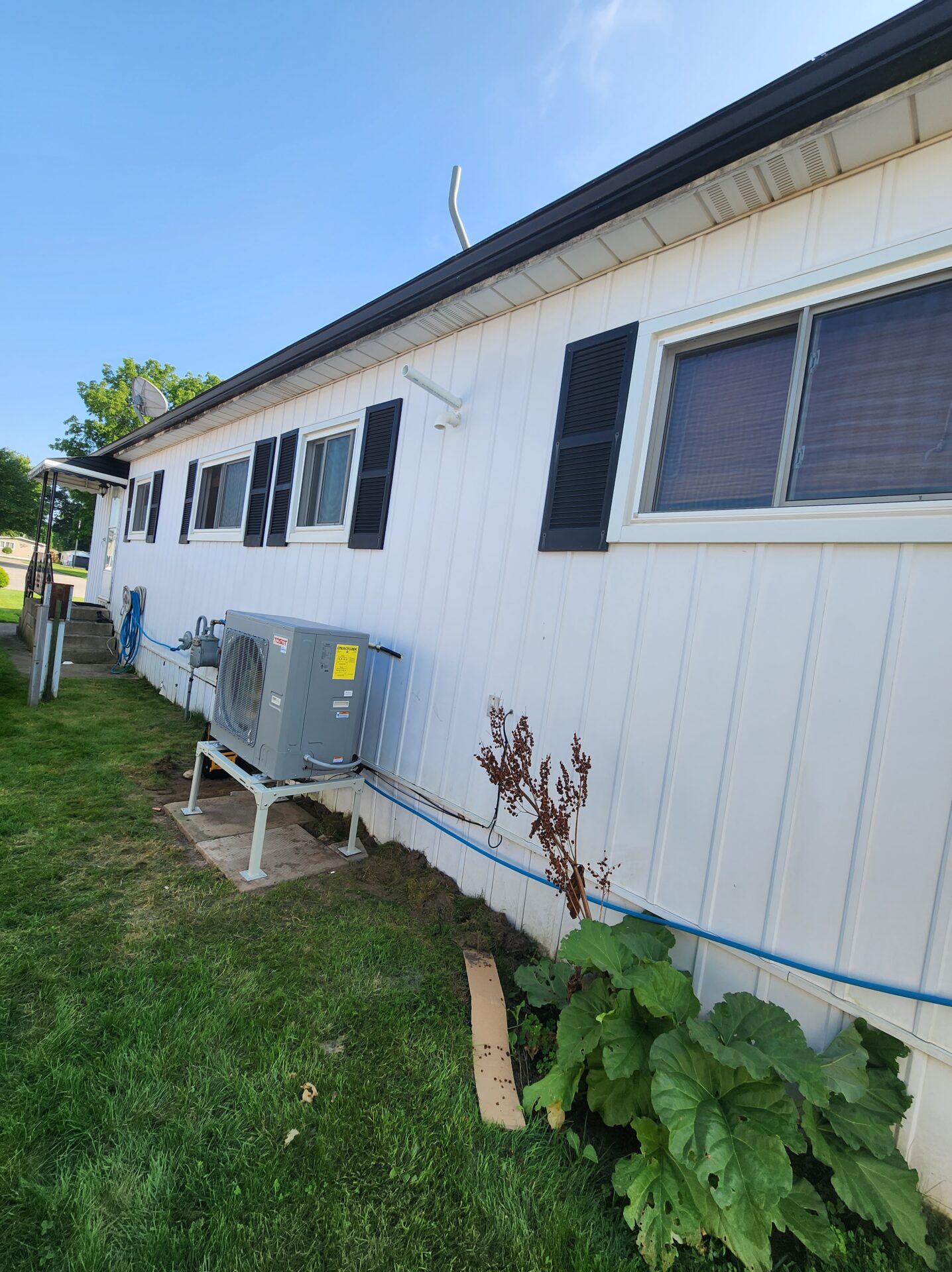 A newly installed side-discharge heat pump mounted on a snow stand next to a residential home.