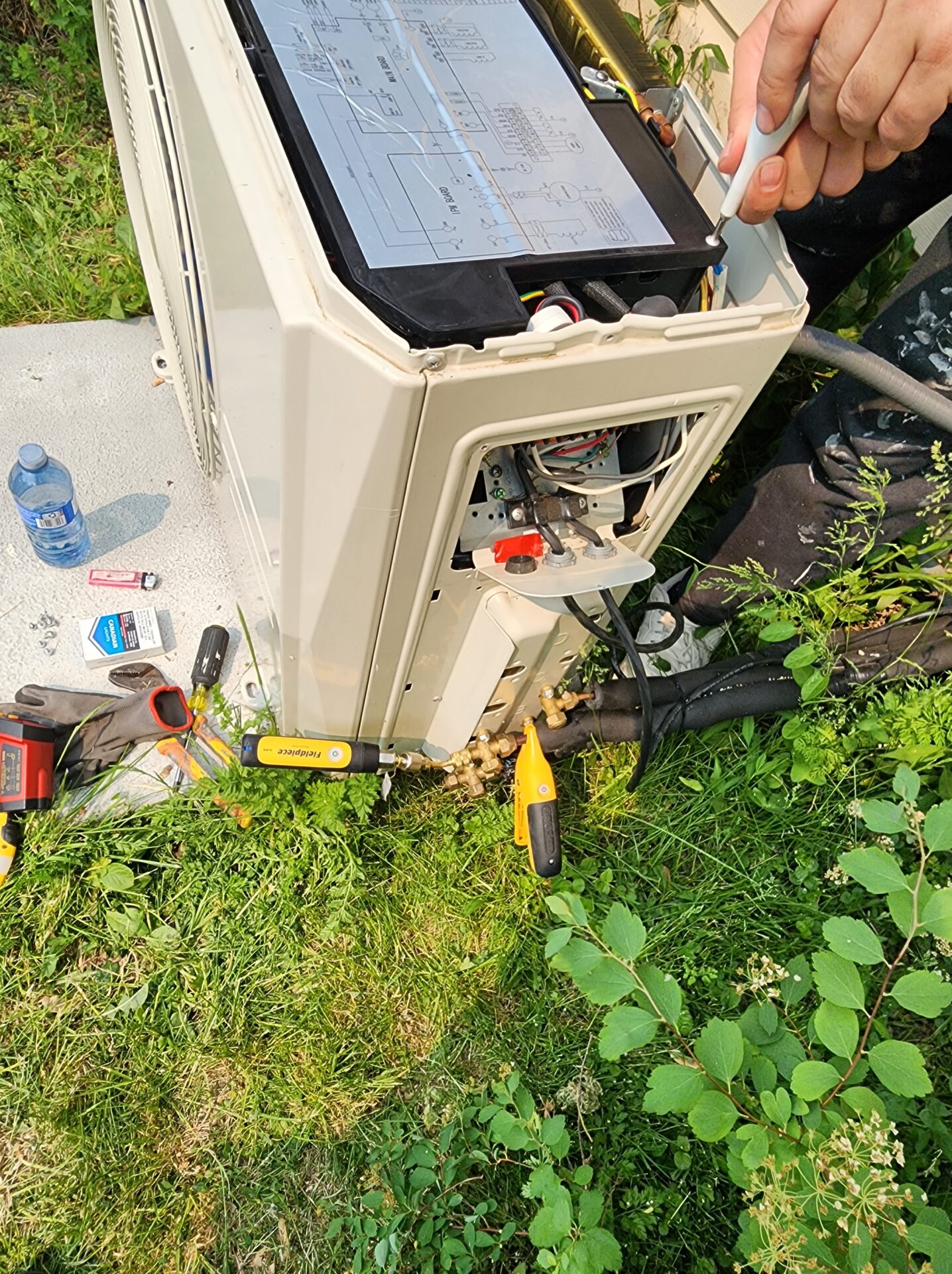 Technician checking internal wiring and testing pressures on a side-discharge heat pump using wireless probes.