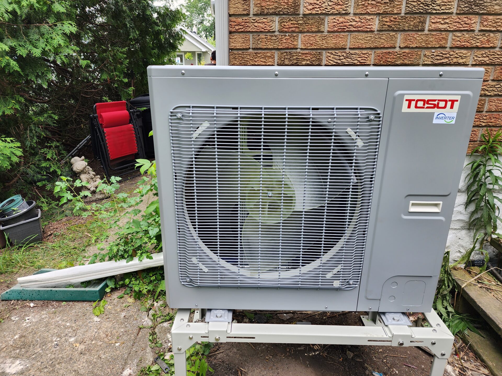 A newly installed, energy-efficient TOSOT inverter heat pump outdoor compressor unit mounted on a custom stand next to a brick wall.