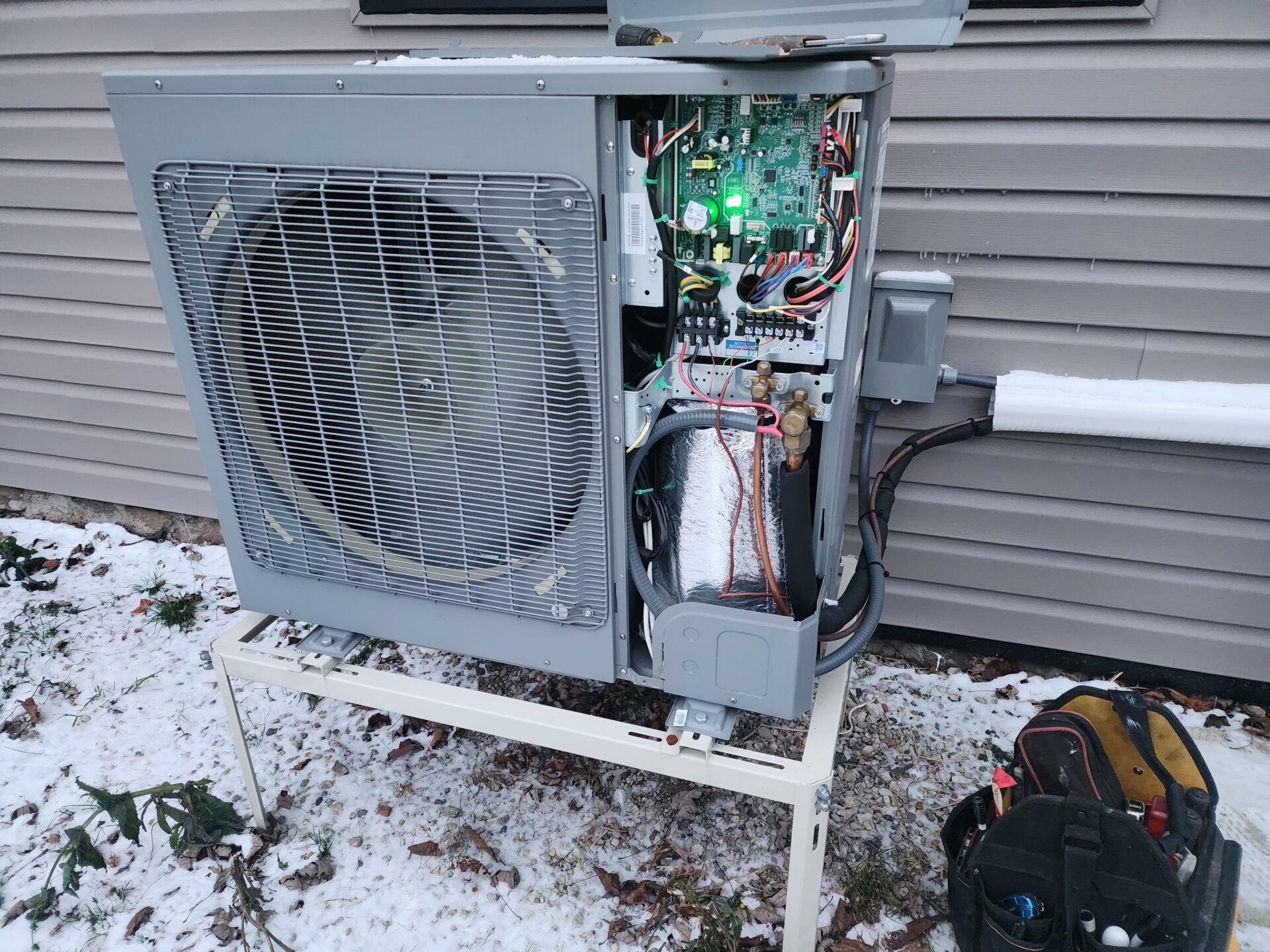 Open side panel of a heat pump showing the electronic control board during a winter HVAC service call.