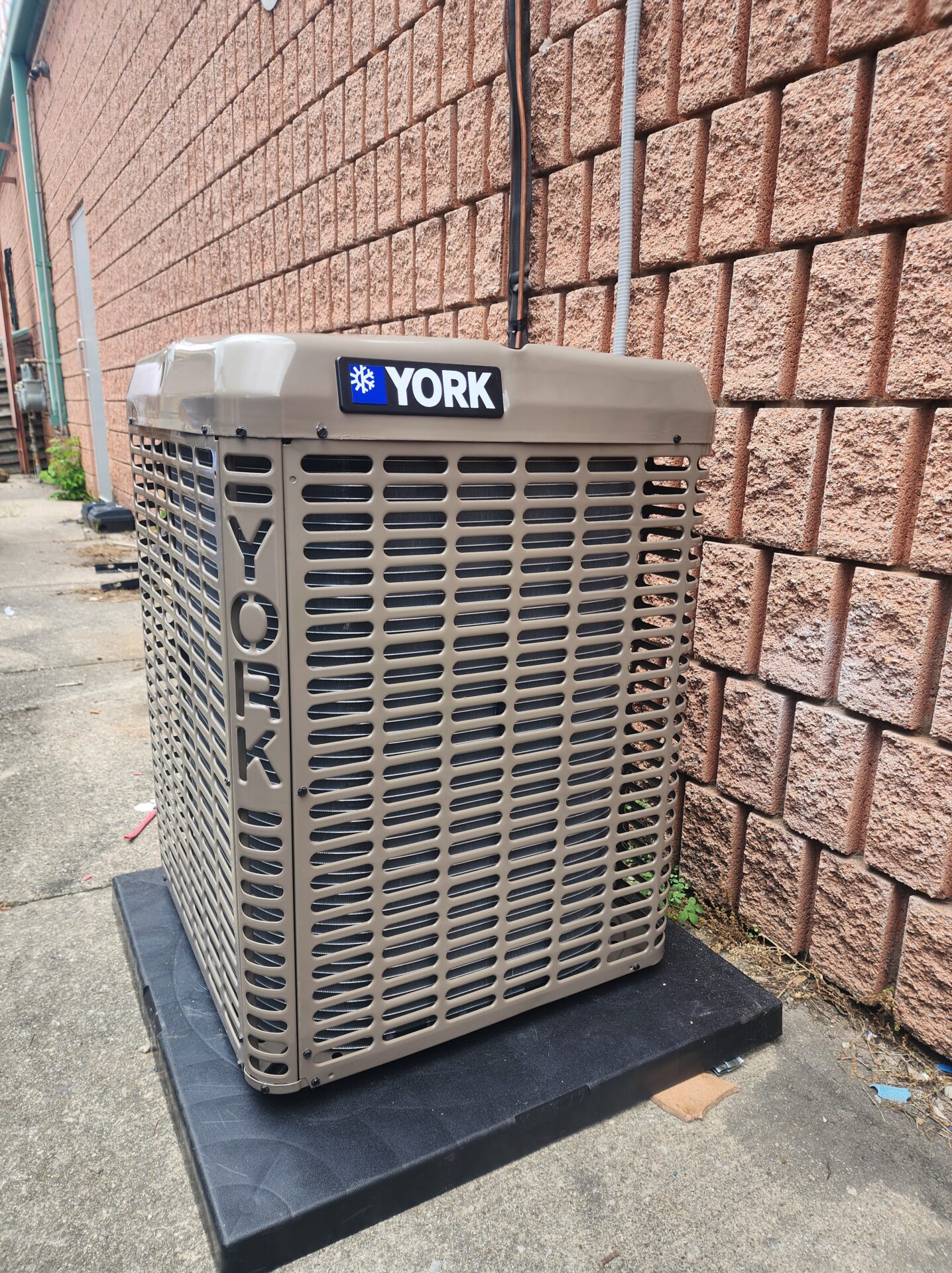 A brand new York central air conditioning condenser unit installed properly on a black equipment pad outside a brick building