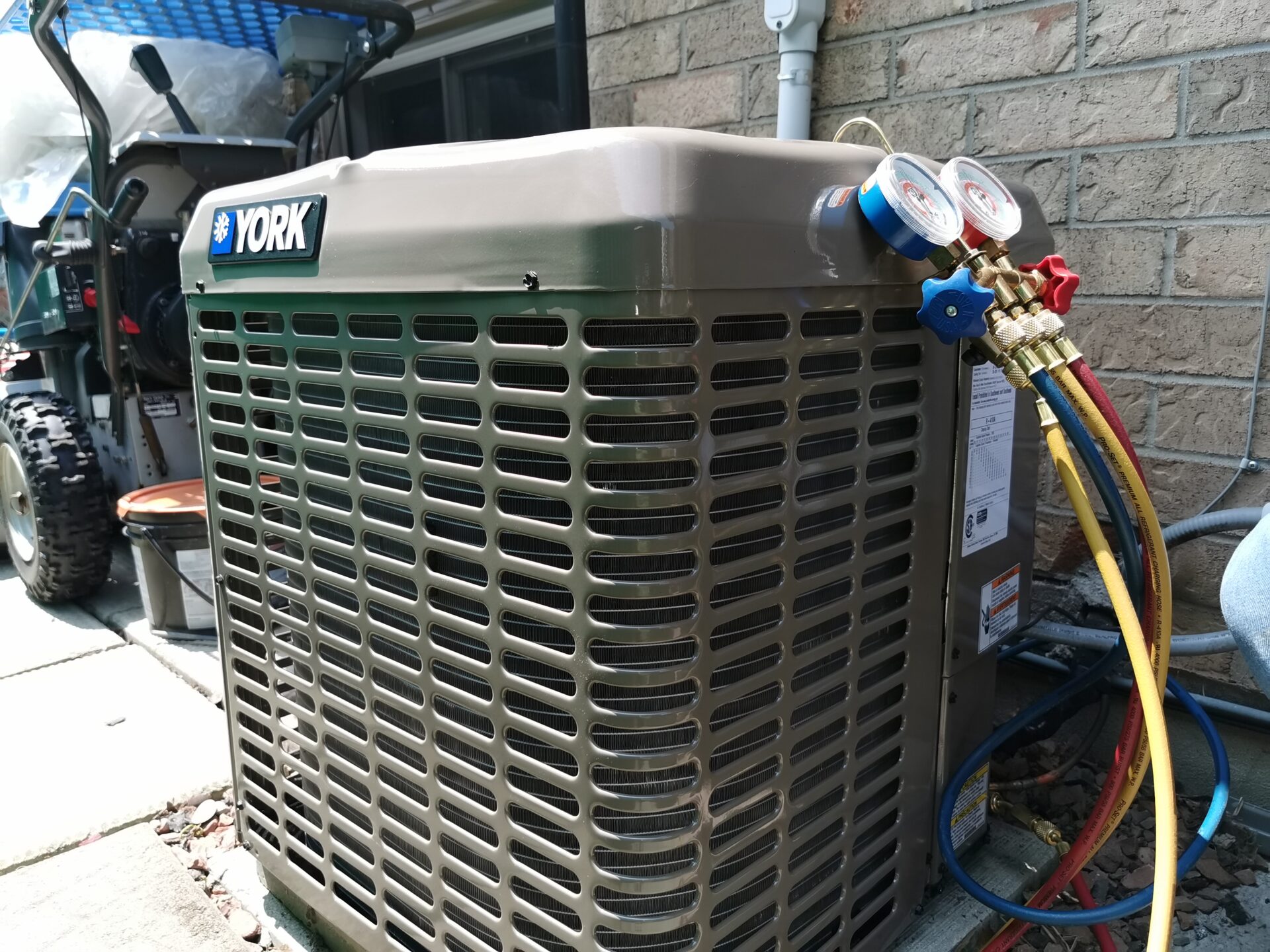 Analog manifold pressure gauges connected to the service valves of a residential York central air conditioning condenser.