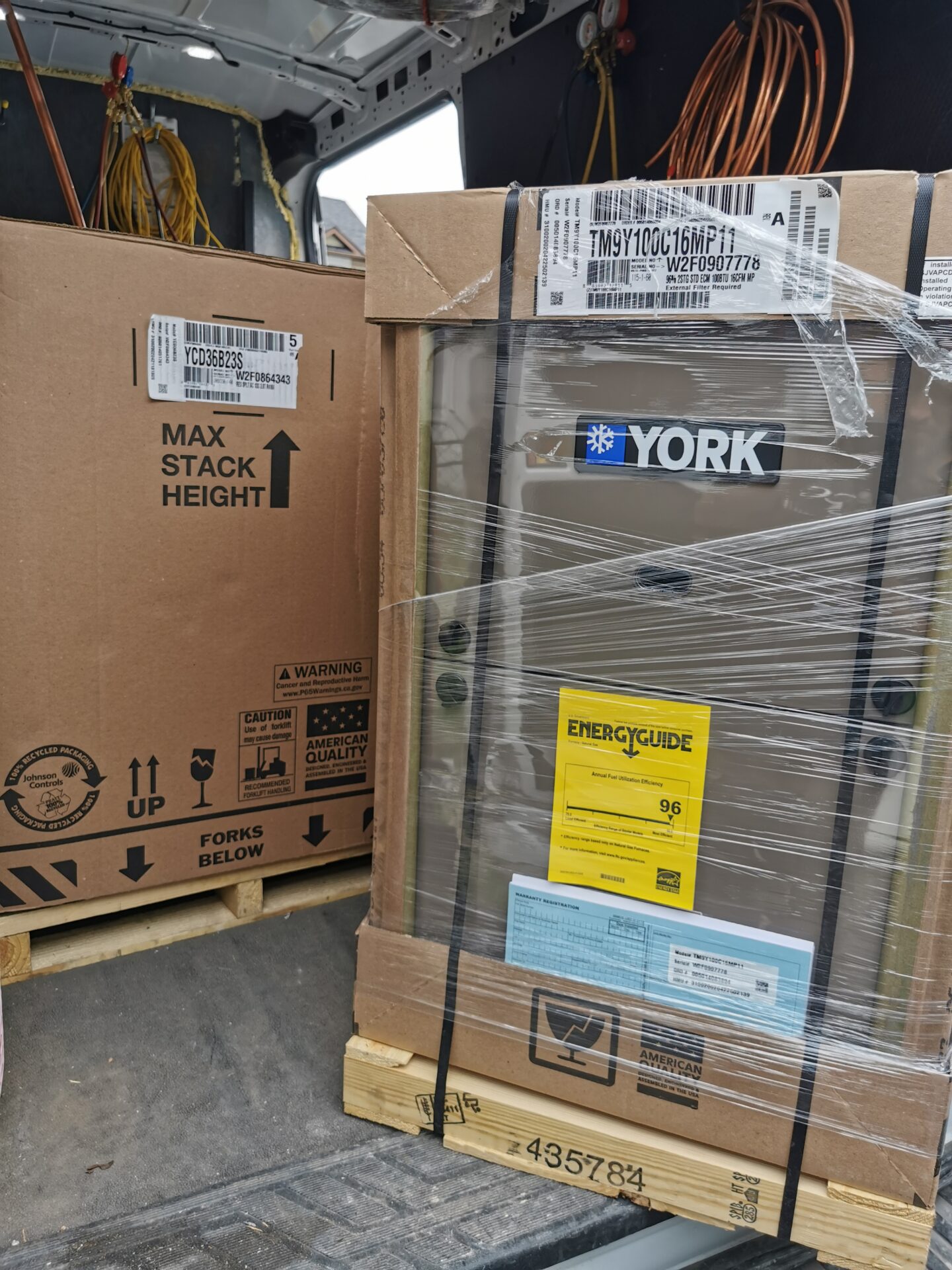 Brand new York high-efficiency gas furnace and central air conditioning unit secured on pallets inside an HVAC service vehicle.